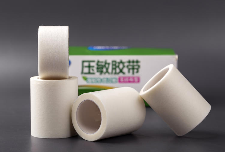 多卷白色医用胶带卷堆叠，背景可见印有「压敏胶带」字样的包装盒；外包装标识与卷芯标签是区分医用与普通胶带的第一道核对项